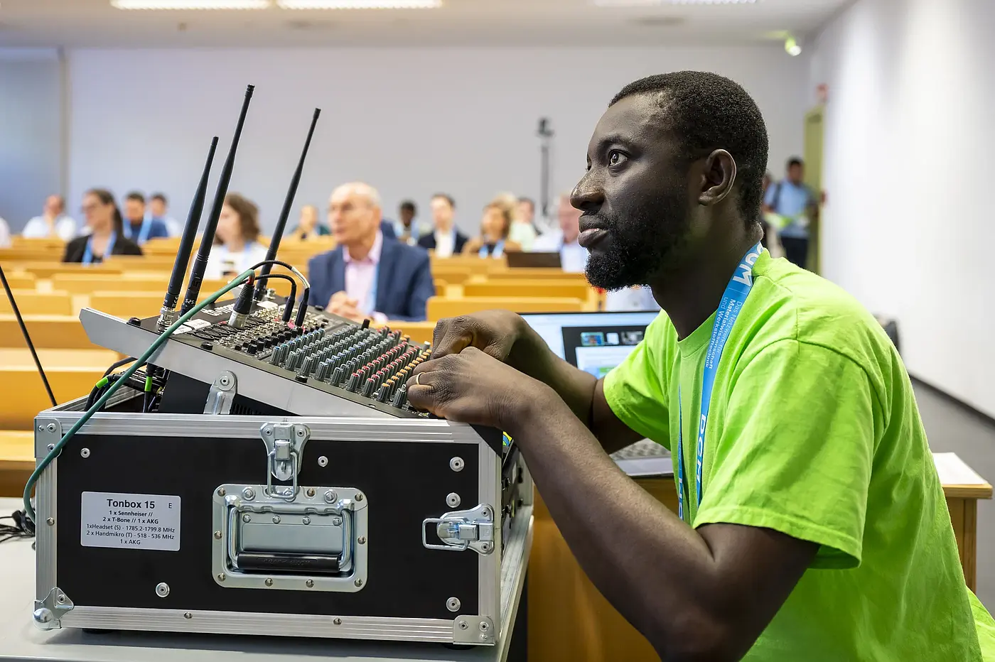 An audio technician manages the mixing desk and wireless microphones in the conference room